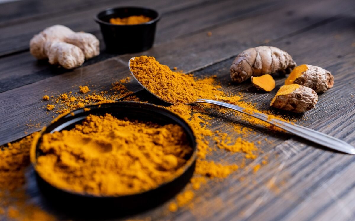 Pó de açafrão vibrante e raiz organizados em superfície de madeira rústica, exibindo ingredientes de tempero culinário