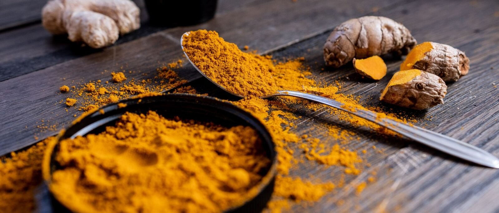 Pó de açafrão vibrante e raiz organizados em superfície de madeira rústica, exibindo ingredientes de tempero culinário