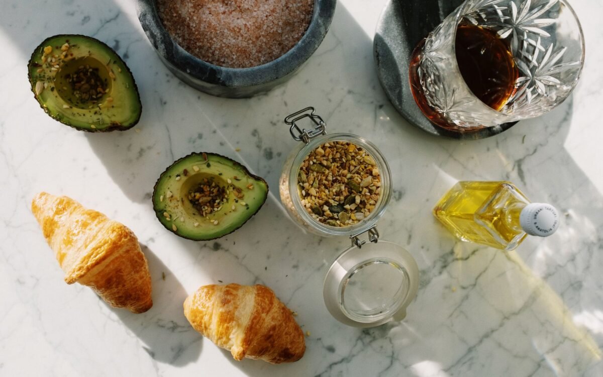 Composição plana de café da manhã nutritivo com abacate, croissants e sementes sobre mármore