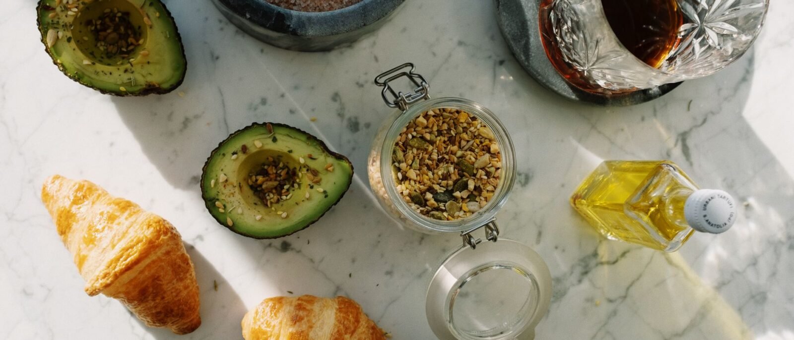 Composição plana de café da manhã nutritivo com abacate, croissants e sementes sobre mármore