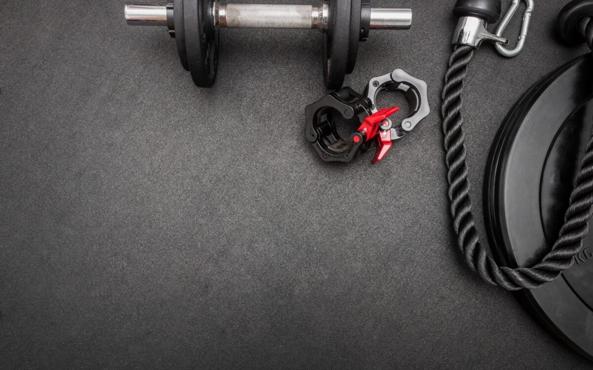 Composição plana de equipamentos de academia incluindo haltere, pesos e corda sobre superfície escura ideal para temas de fit