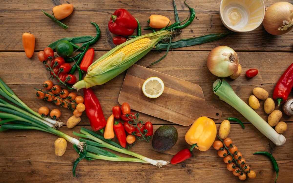 Sortido colorido de vegetais e frutas frescos organizados em uma mesa de madeira com tábua de corte