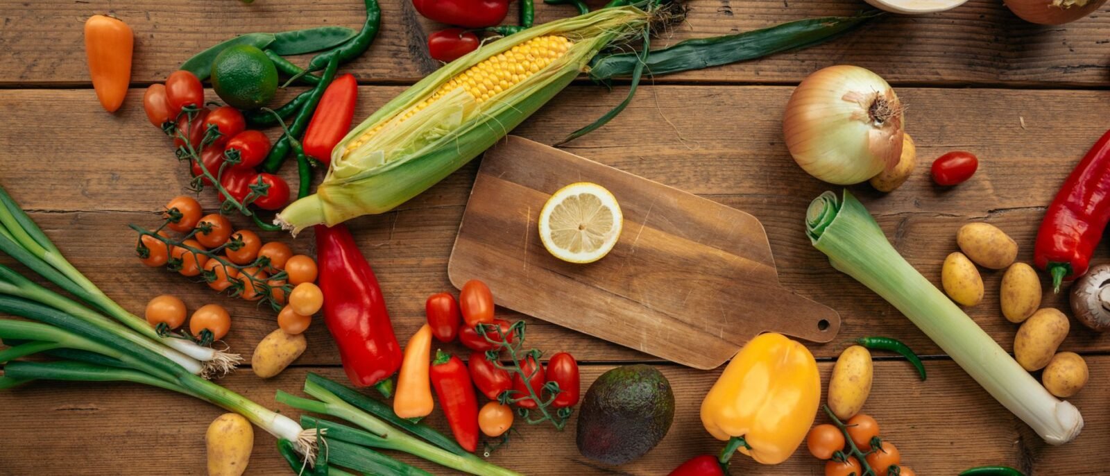 Sortido colorido de vegetais e frutas frescos organizados em uma mesa de madeira com tábua de corte
