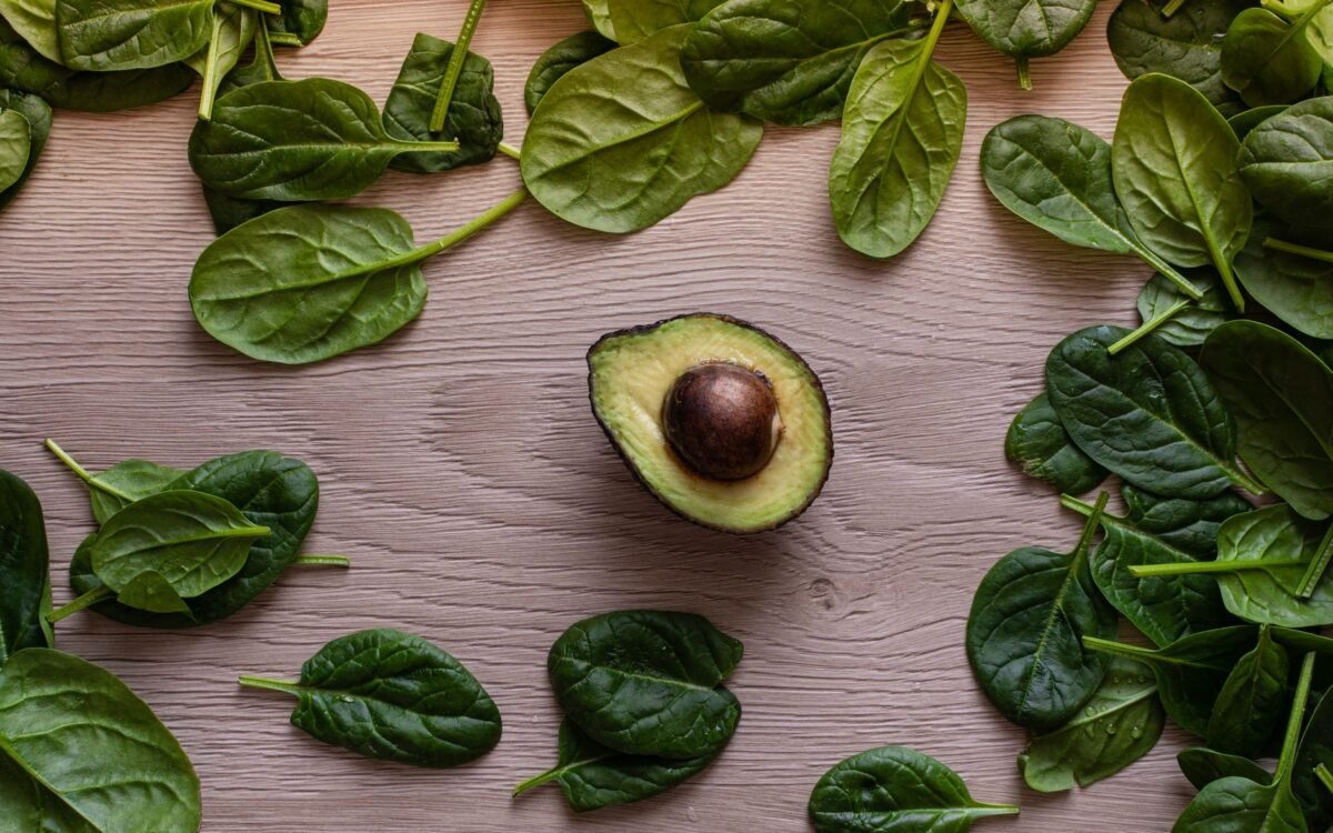 Composição de abacate fresco e folhas de espinafre em mesa de madeira, ideal para conceitos de alimentação saudável