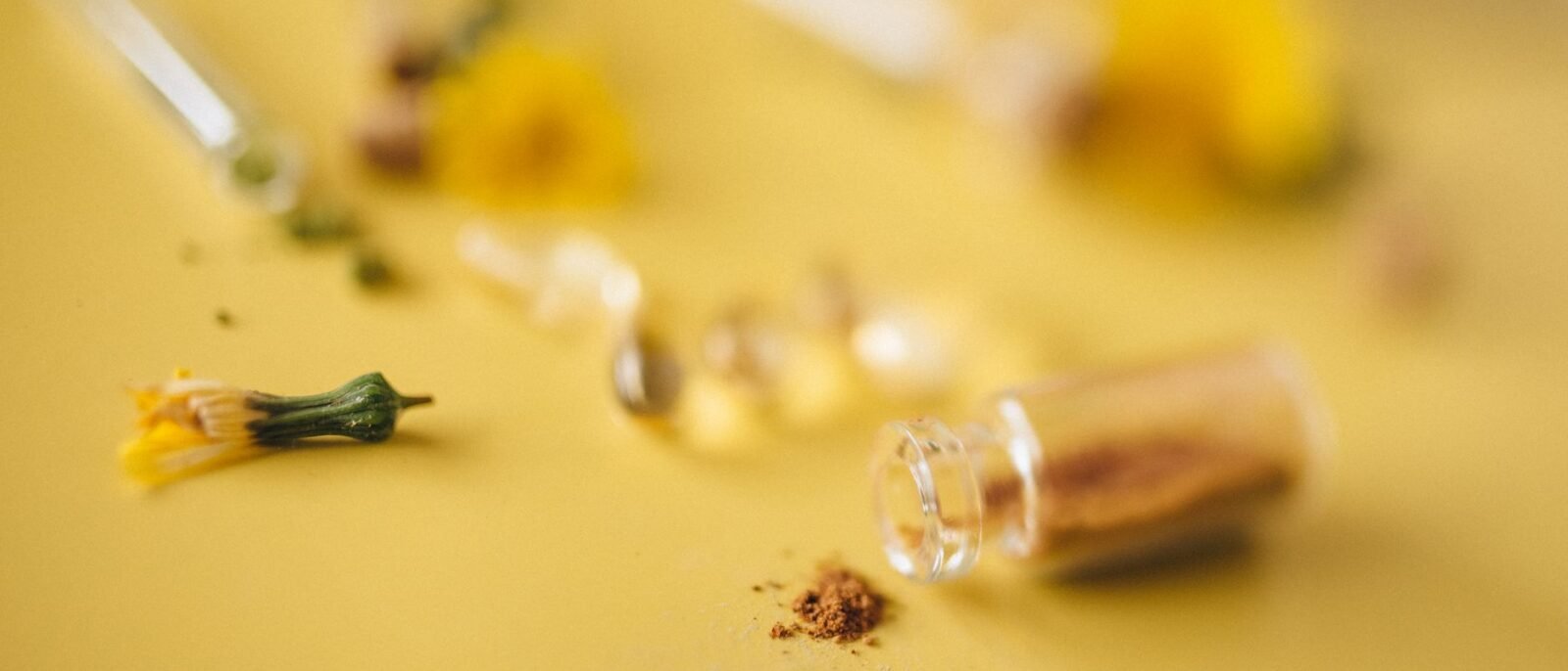 Detalhe de pó herbal e flores sobre superfície amarela, conceito de remédios naturais
